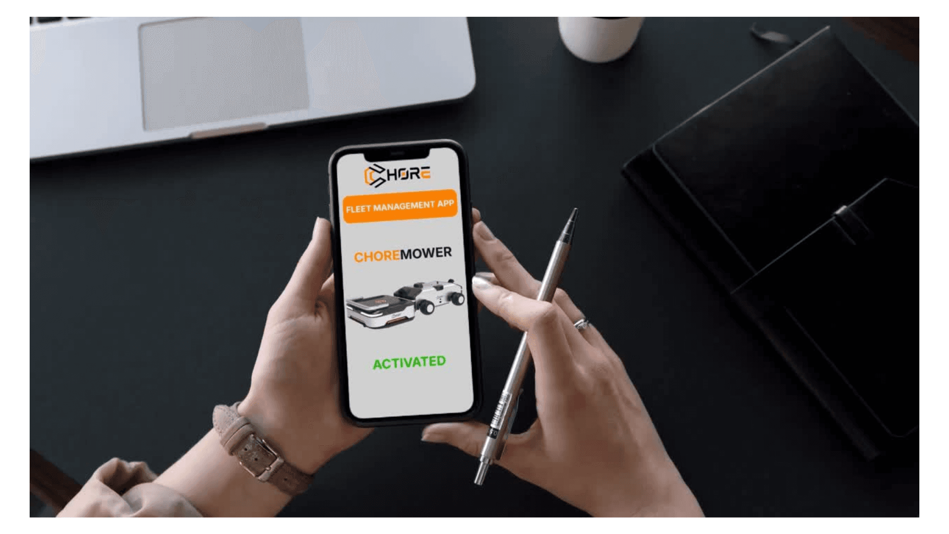 Hands holding a smartphone displaying the CHORE Fleet Management App with live mower status
